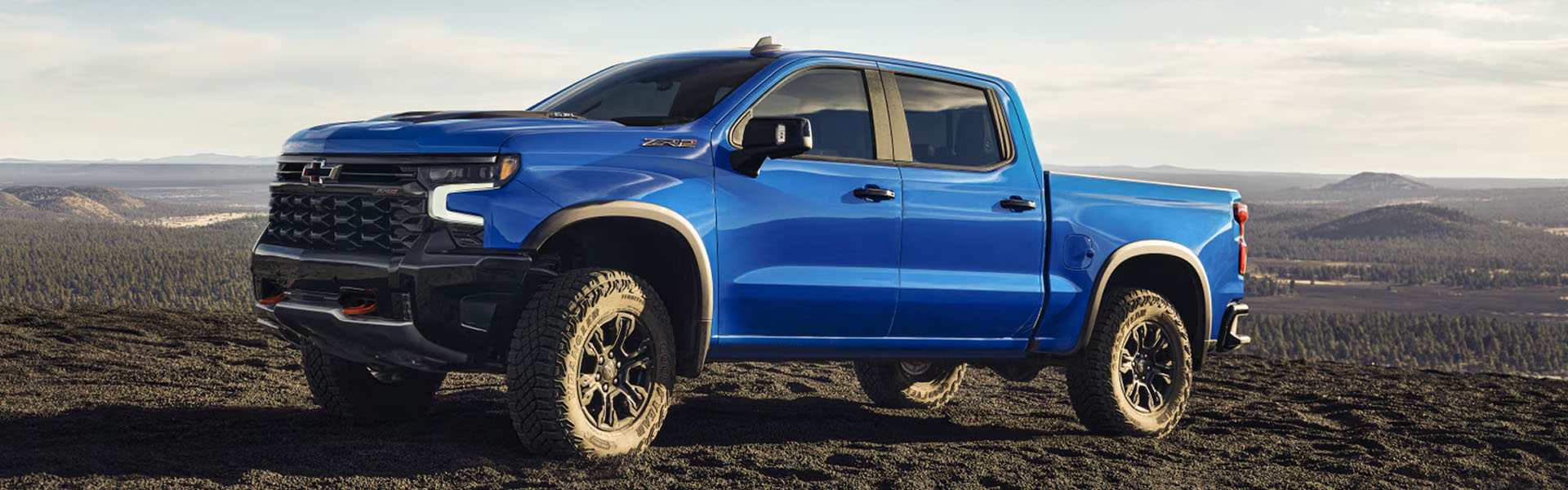 A blue Chevrolet Silverado ZR2 truck parked on rugged terrain with a mountainous background.